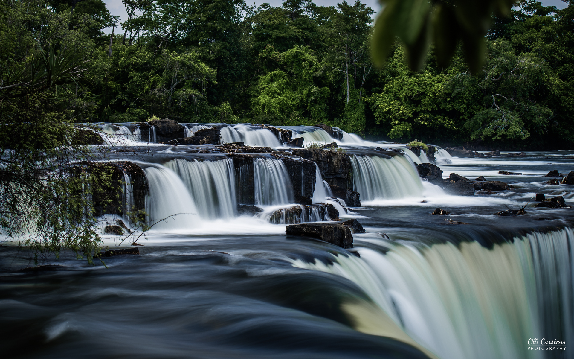 Lumangwe Falls im Nordosten Sambias. Exotische Destinationen mit Buschmann Safaris besuchen. Kaskaden von Wasserfällen, umgeben von üppigem Grün und ruhigem Wasser.