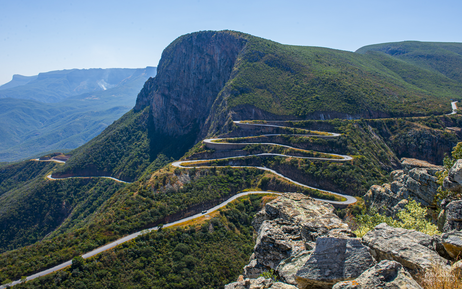 Der berühmte Leba Pass: Angola erleben Kurvenreiche Straße entlang einer Berglandschaft mit grünen Hügeln und klarem Himmel.